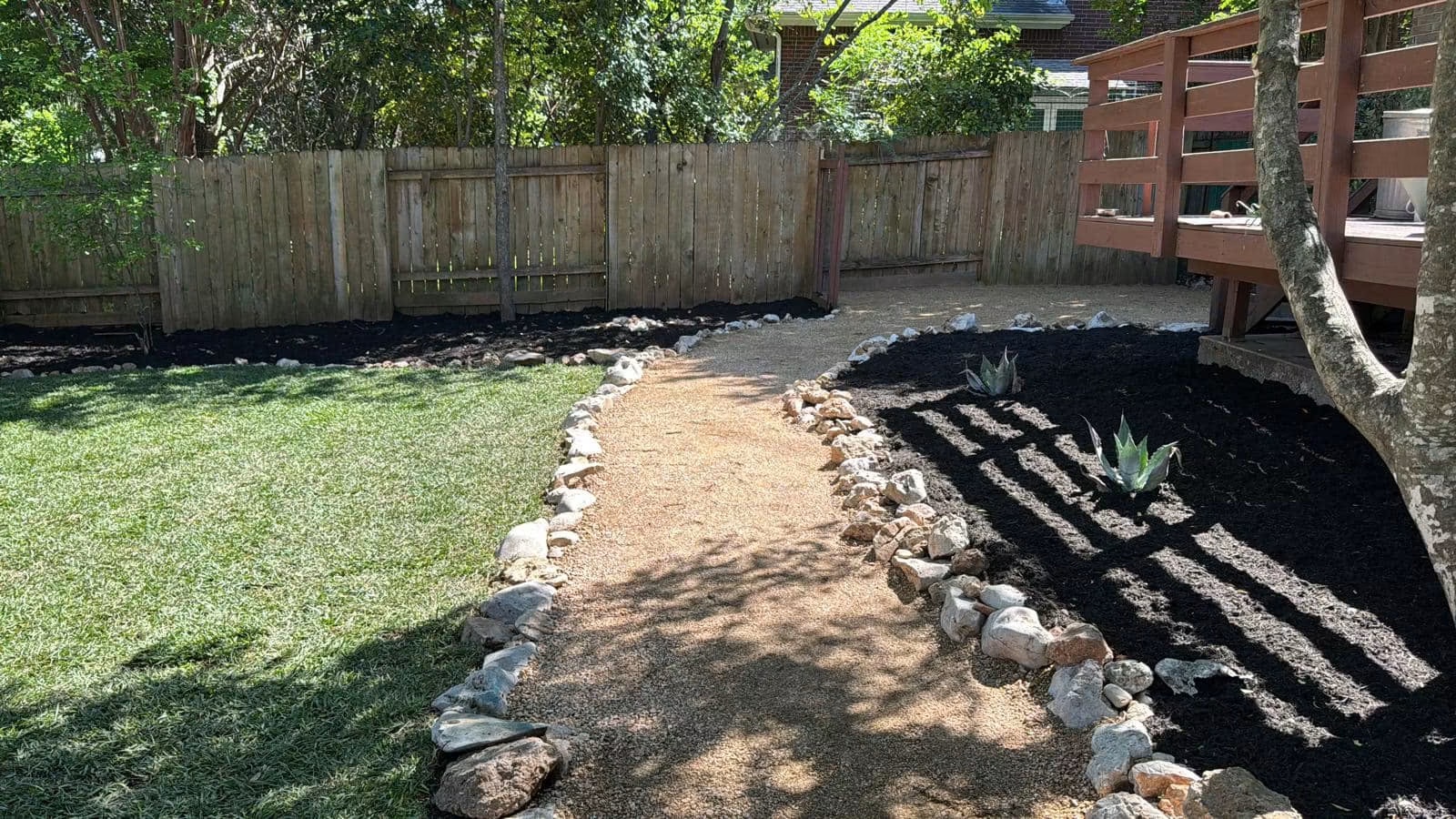 Completed residential backyard gravel path with stone borders and mulched planting beds